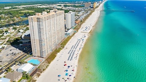Ein Hochhaus-Hotel mit mehreren Stockwerken, ein Strand mit Sonnenschirmen und freier Sicht auf den Ozean.