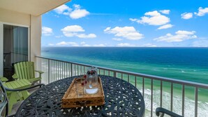 A balcony with a view of the ocean, a table with a tray, and green chairs.