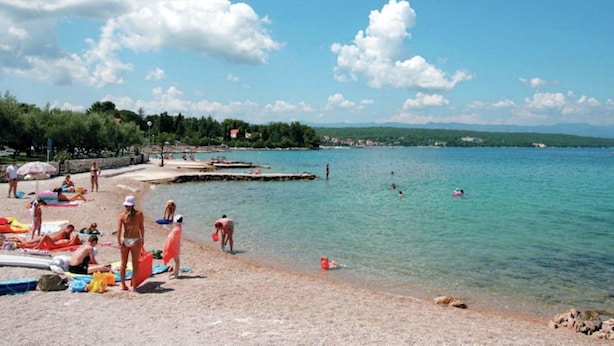 Una spiaggia con acque cristalline, persone che prendono il sole e una costa in lontananza.