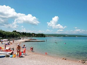 A beach with clear water, people sunbathing, and a distant shoreline. - Apartment in Malinska With Terrace (Malinska-Dubasnica)