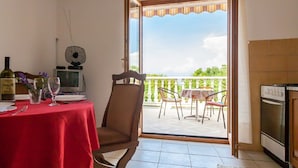 Zona pranzo con tavolo rosso, sedie, una ventola e vista sull'esterno.