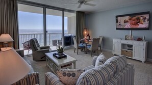 A spacious living room with a balcony overlooking the ocean, a television mounted on the wall, and a dining area with a table and chairs. - BEAUTIFUL BEACHFRONT! 1 MILE W OF PIER PARK! (Panama City Beach)