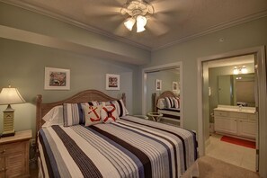 Un dormitorio con cama, mesita de noche, cómoda, ventilador de techo y baño con espejo y lavamanos.