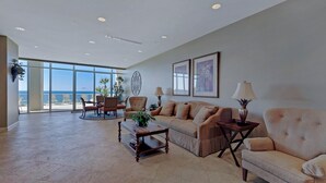 A spacious living room with a large window offering a view of the ocean, a sofa set, a coffee table, and a side table with a lamp. - BEAUTIFUL BEACHFRONT! 1 MILE W OF PIER PARK! (Panama City Beach)
