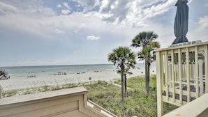 A beach view from a balcony with a railing, palm trees, and a statue.