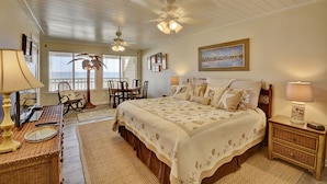 A bedroom with a large bed, a ceiling fan, a desk with a lamp, and a chair.