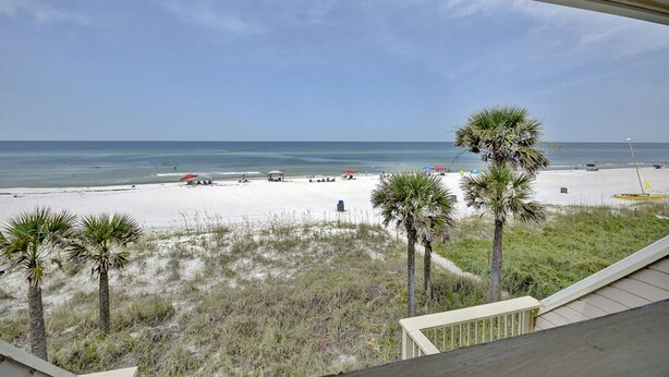 A beach view from a balcony with palm trees and a clear sky.