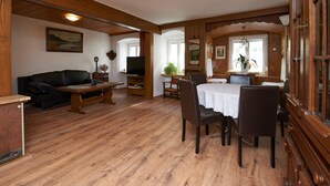 A cozy living room with a wooden floor, a sofa, a TV, and a dining area with chairs and a table. - Spacious apartment in the old town, 90 sqm, 1st sep. Bedroom (Wasserburg am Inn)