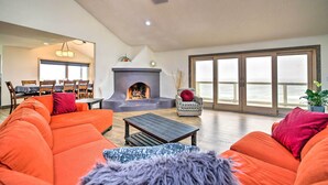A spacious living room with a fireplace, orange sofas, a dining area, and a large sliding glass door to the outside. - Luxurious Newport Estate w/ Spa & Lighthouse Views (Newport)