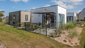 Ein modernes, zweistöckiges Haus mit überdachter Terrasse, umzäunter Garten und blauem Himmel.