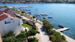 Una marina con barcos amarrados, una carretera que lleva a un edificio blanco de techo rojo, y un cielo azul despejado.