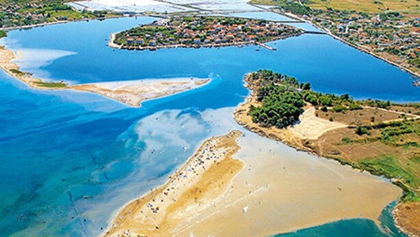 Vista aérea de una zona costera con una gran bahía, una pequeña isla con edificios y una playa de arena.