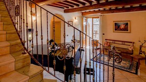 A grand staircase with ornate balusters leading to a living area with a piano, a sofa, and a rug. - Luxurious Villa in Cortona Tuscany with Hot Tub (Cortona)