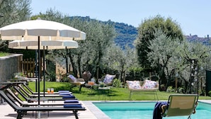 A poolside area with lounge chairs, umbrellas, and a view of a mountainous landscape. - Luxurious Villa in Cortona Tuscany with Hot Tub (Cortona)