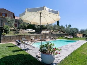 A poolside area with lounge chairs, a large umbrella, and a potted plant. - Luxurious Villa in Cortona Tuscany with Hot Tub (Cortona)