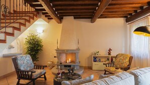 A cozy living room with a fireplace, wooden staircase, and comfortable seating. - Luxurious Villa in Cortona Tuscany with Hot Tub (Cortona)