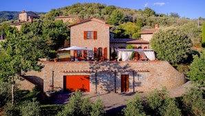 A stone villa with a red garage door, surrounded by lush greenery and hills. - Luxurious Villa in Cortona Tuscany with Hot Tub (Cortona)