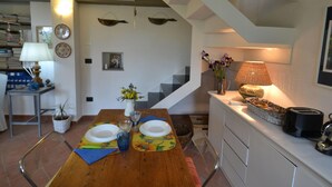 Un comedor con una mesa de madera preparada para dos, una cocina con armarios blancos y una escalera que sube a un nivel superior.