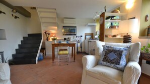 Una sala de estar con un sofá, una silla, una mesa de comedor y una zona de cocina al fondo.