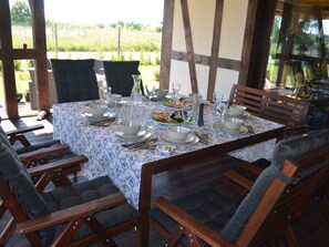 Un espace extérieur aménagé pour les repas, avec une table dressée pour six personnes, entourée de chaises en bois.