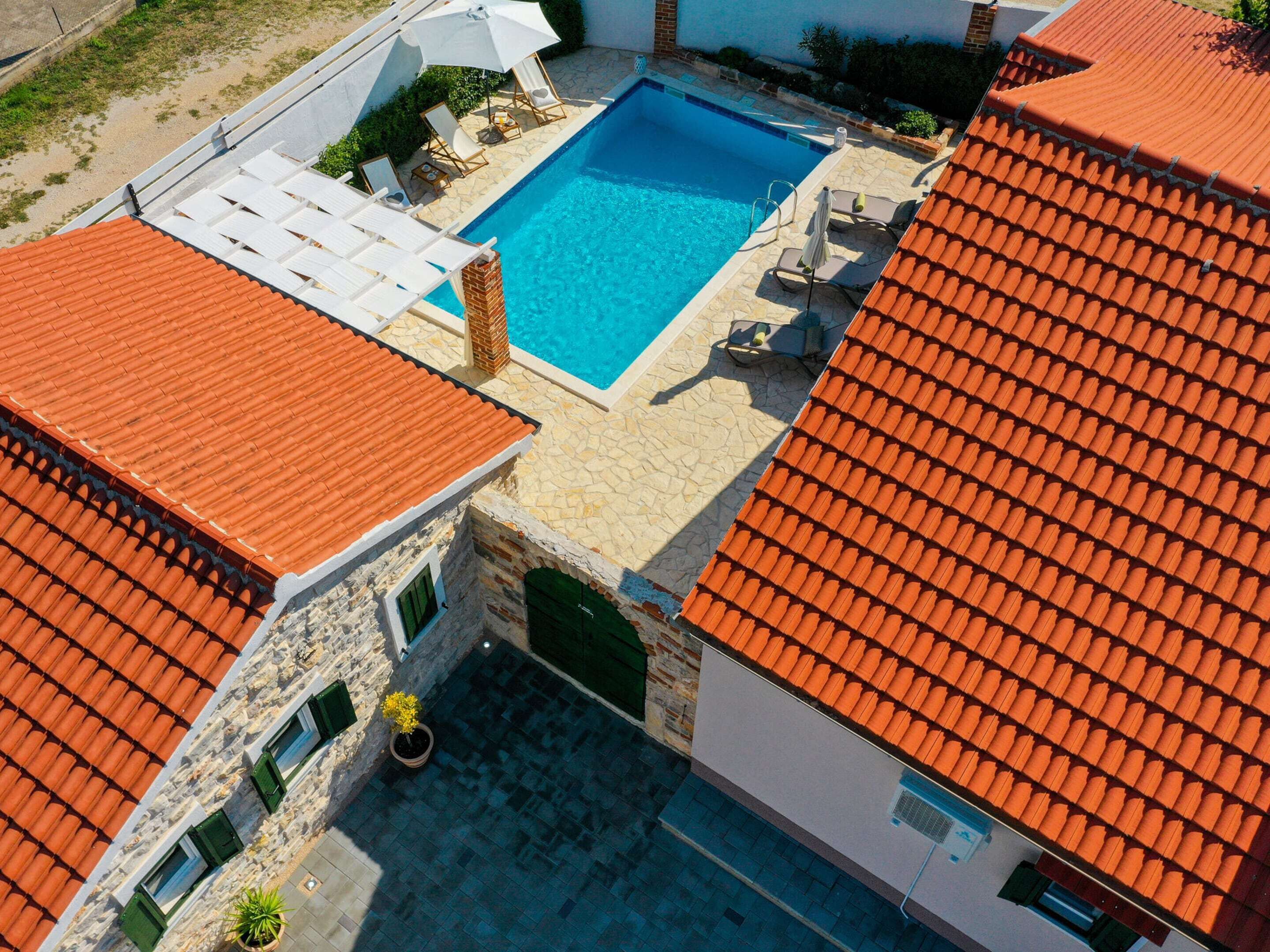 Une piscine sur le toit, avec une terrasse en pierre, entourée d’immeubles aux toits recouverts de tuiles rouges.