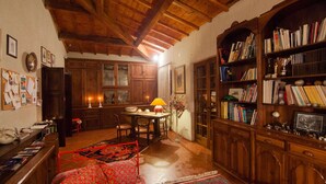 A cozy living room with wooden beams, a bookshelf, a dining area, and a red sofa. - Tuscan Castle View Grand Villa (Castiglion Fiorentino)
