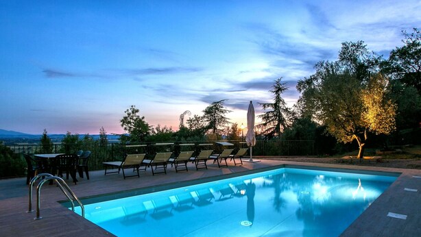 A rectangular swimming pool with a wooden deck, surrounded by lounge chairs and tables. - Tuscan Castle View Grand Villa (Castiglion Fiorentino)