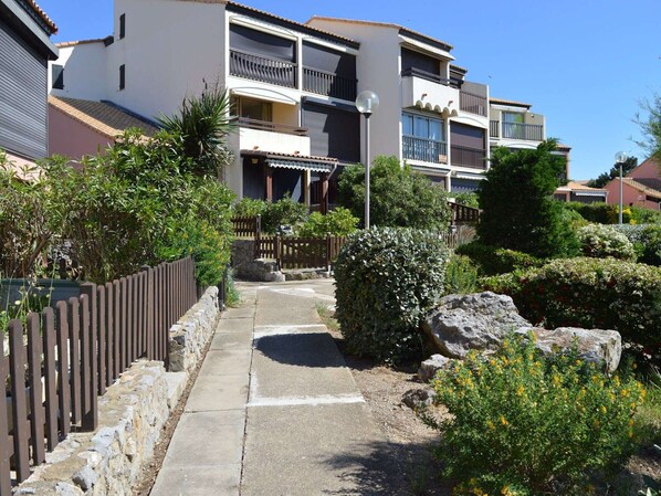 A residential building with multiple balconies, a paved pathway, and surrounding greenery.