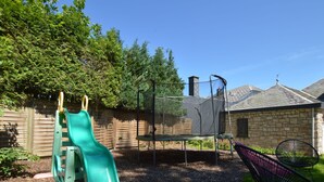 A playground with a slide and trampoline, surrounded by a wooden fence and trees. - Waimes Wellness & Nature Villa (Waimes)