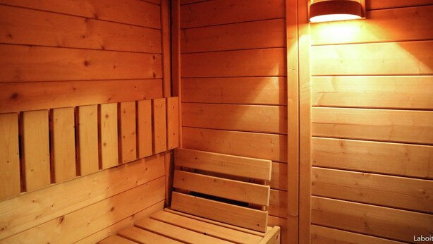 A wooden sauna with benches and a wall-mounted light fixture. - Waimes Wellness & Nature Villa (Waimes)