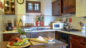 A kitchen with wooden cabinets, a microwave, a stove, and a sink. There is a clock on the wall and a vase with flowers on the counter. - Elegant Villa Near Cortona (Cortona)
