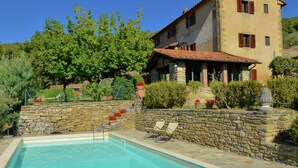 A pool area with stone walls and a pool, surrounded by a stone building with a tiled roof and windows. - Elegant Villa Near Cortona (Cortona)