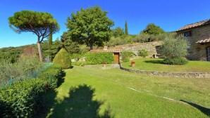 A stone building with a tiled roof, surrounded by a well-maintained garden with various shrubs and trees. - Elegant Villa Near Cortona (Cortona)