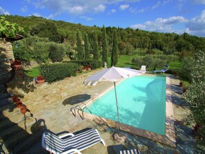 A swimming pool with a stone deck, surrounded by potted plants and a view of a lush green hillside. - Elegant Villa Near Cortona (Cortona)