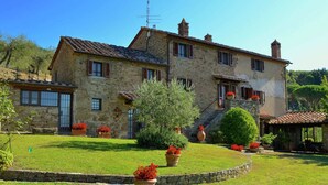 A stone building with multiple windows and a well-maintained lawn with potted plants. - Elegant Villa Near Cortona (Cortona)