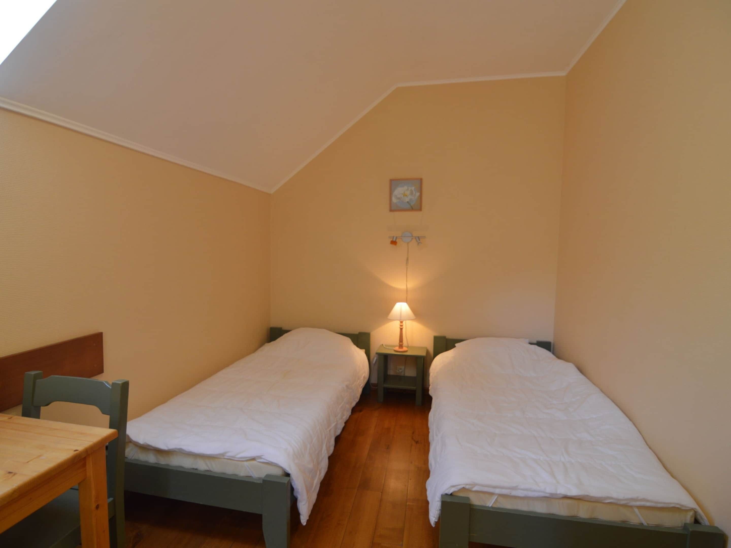 A small, cozy room with two single beds, a wooden table, and a lamp.