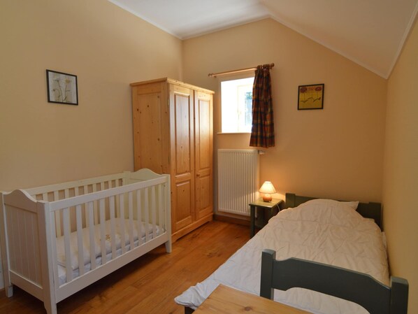 A bedroom with a crib, a bed, a wardrobe, a radiator, and a window with curtains.