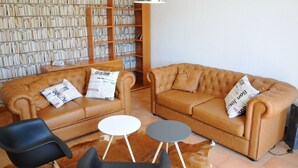 A living room with a brown leather sofa, two black chairs, a white coffee table, and a bookshelf filled with books. - Holiday Home in Noiseux With Private Hot Tub (Somme-Leuze)