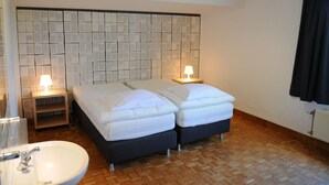A hotel room with two beds, a bedside table with a lamp, a wooden floor, a white sink, and a tiled wall with a pattern. - Holiday Home in Noiseux With Private Hot Tub (Somme-Leuze)