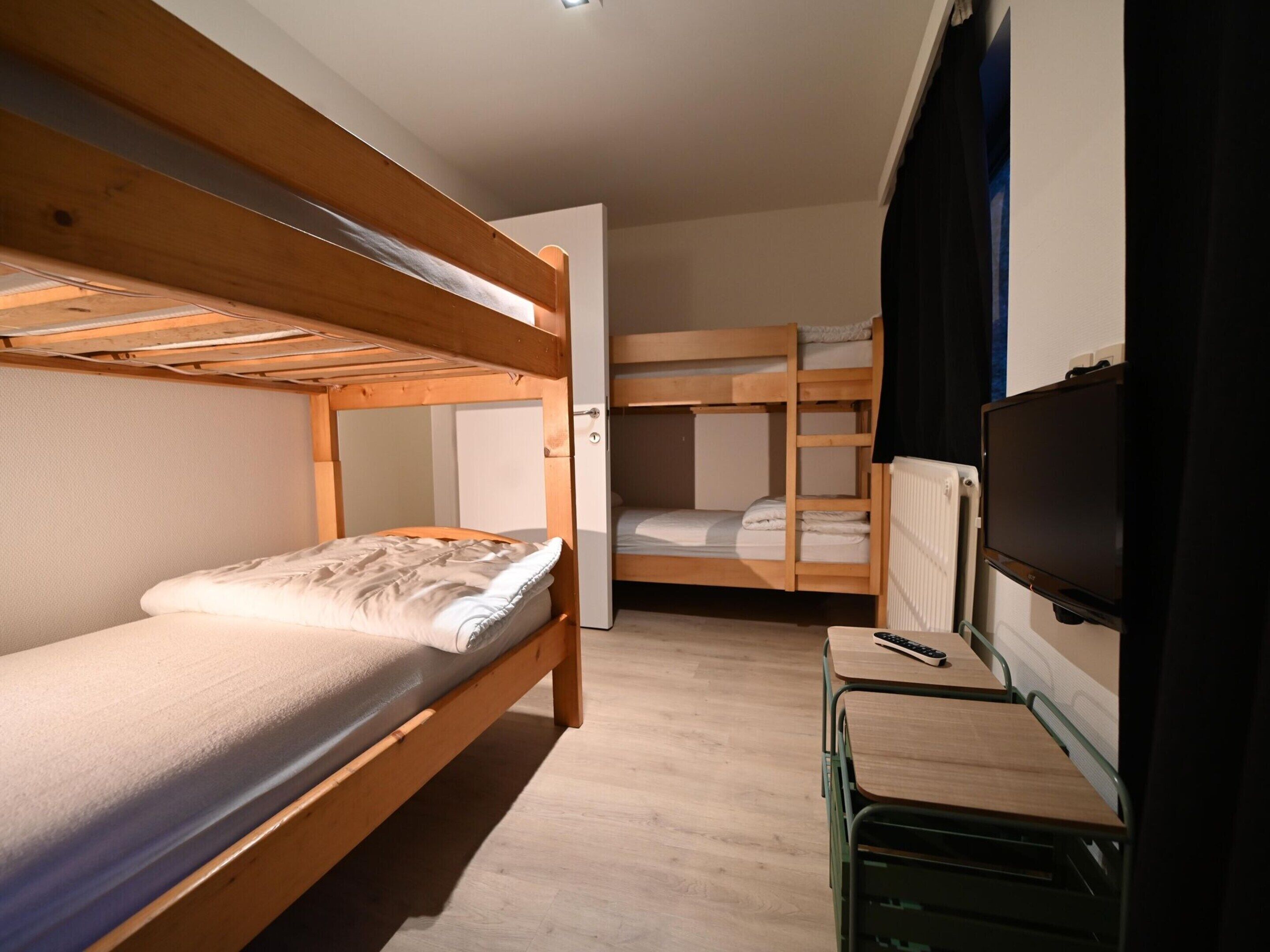 A dormitory room with bunk beds, a desk with a chair, and a television.