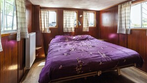 A bedroom with a bed, two windows, a radiator, and a lamp.