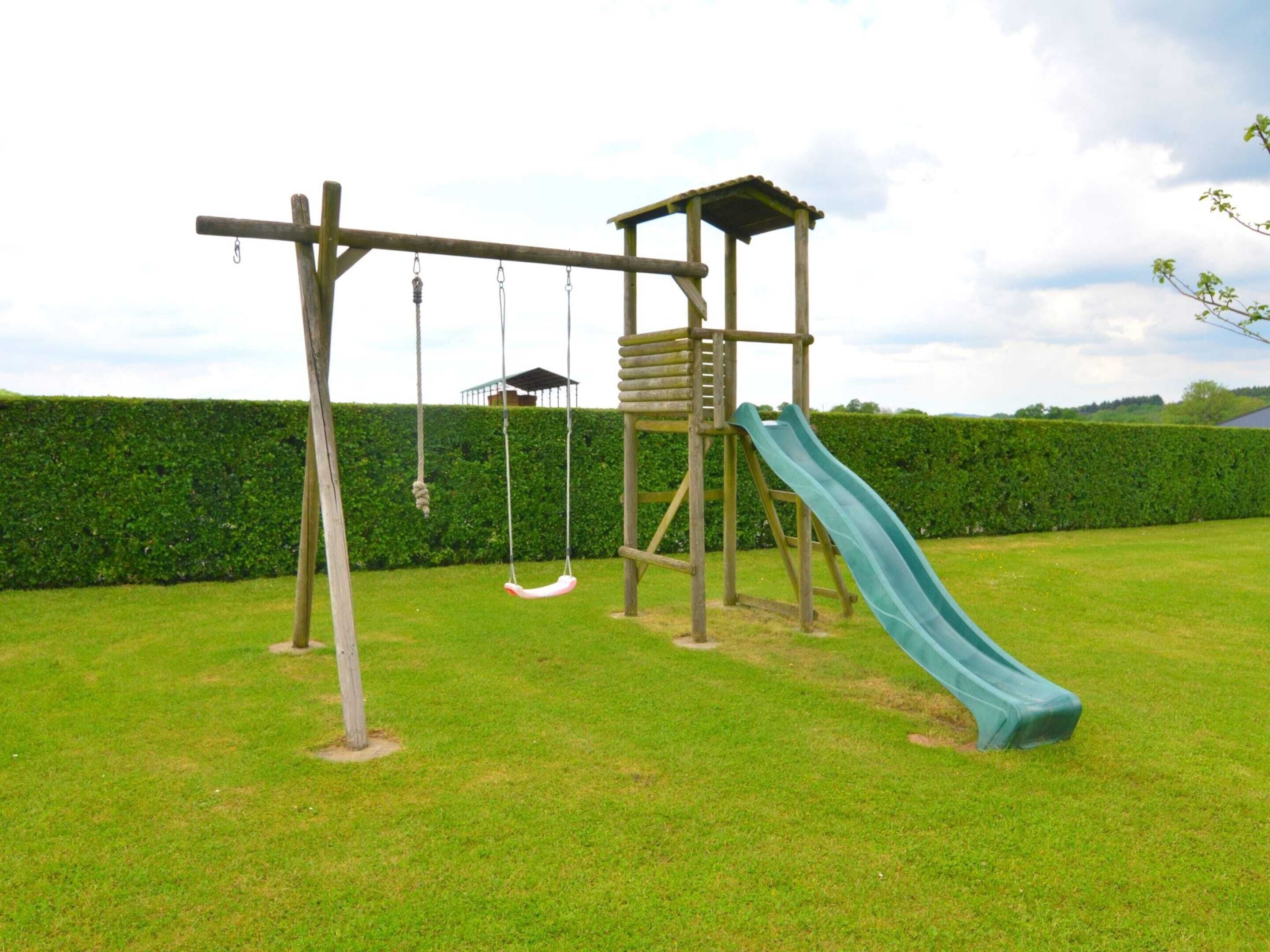 A wooden playground structure with a slide and swings in a grassy area.