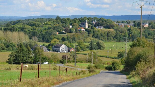 Eine ländliche Straße führt zu einem Dorf mit Kirche und Häusern.
