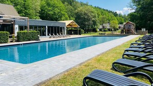 Une piscine avec des chaises longues, une structure de jeux en bois et un bâtiment doté d’un toit en pente.