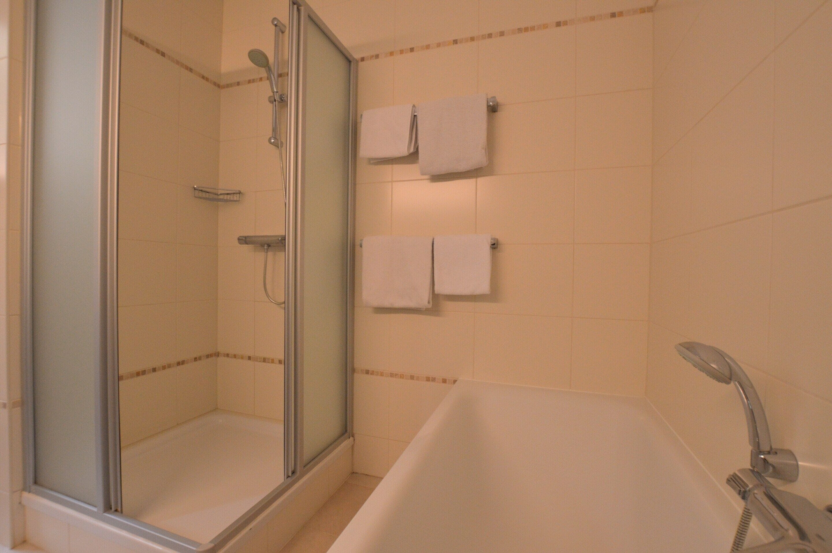 A bathroom with a glass-enclosed shower, a bathtub, and two towels hanging on the wall.