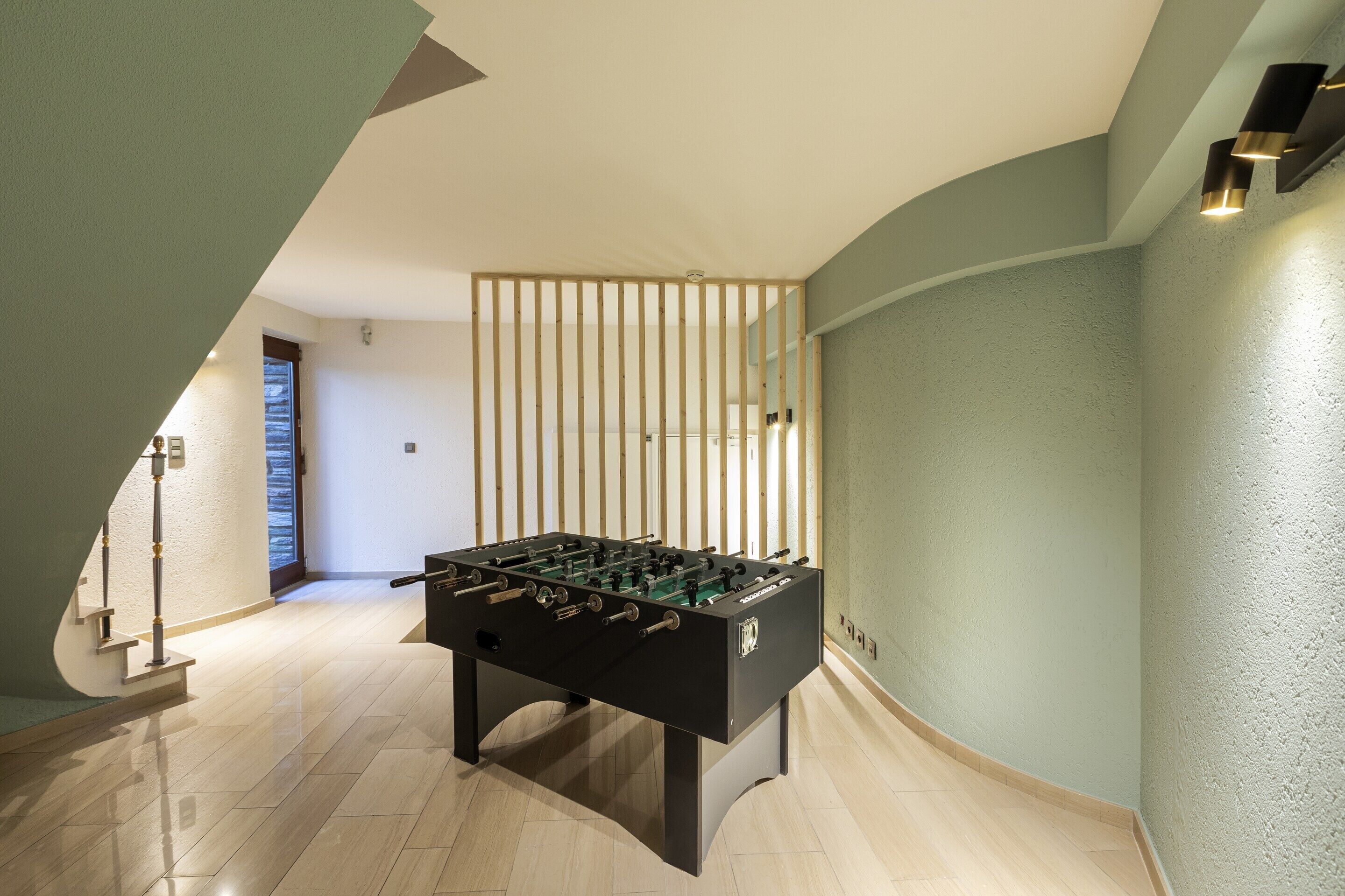 Une pièce moderne avec un baby-foot, un escalier et un mur incurvé.