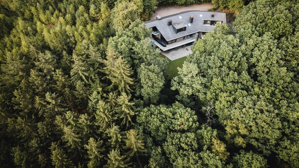 Ilmakuva modernista talosta, jonka ympärillä on tiheä metsä.