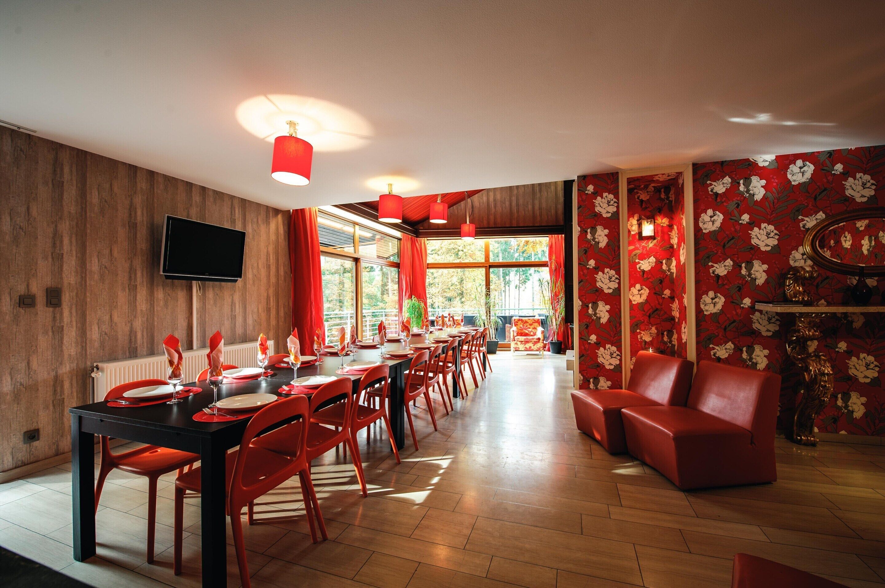 A dining area with a long table, red chairs, and red pendant lights.