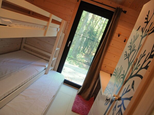 Interior de una cabaña con literas, una puerta que da al exterior y una pared decorada con un motivo de árbol.