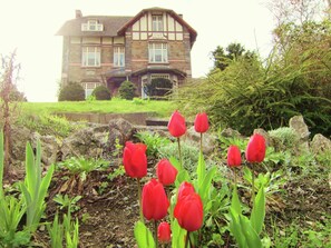 A large stone house with a prominent entrance and a well-maintained garden with red tulips. - A Beautiful Belle Epoque Villa in the Heart of Hamoir (Hamoir)